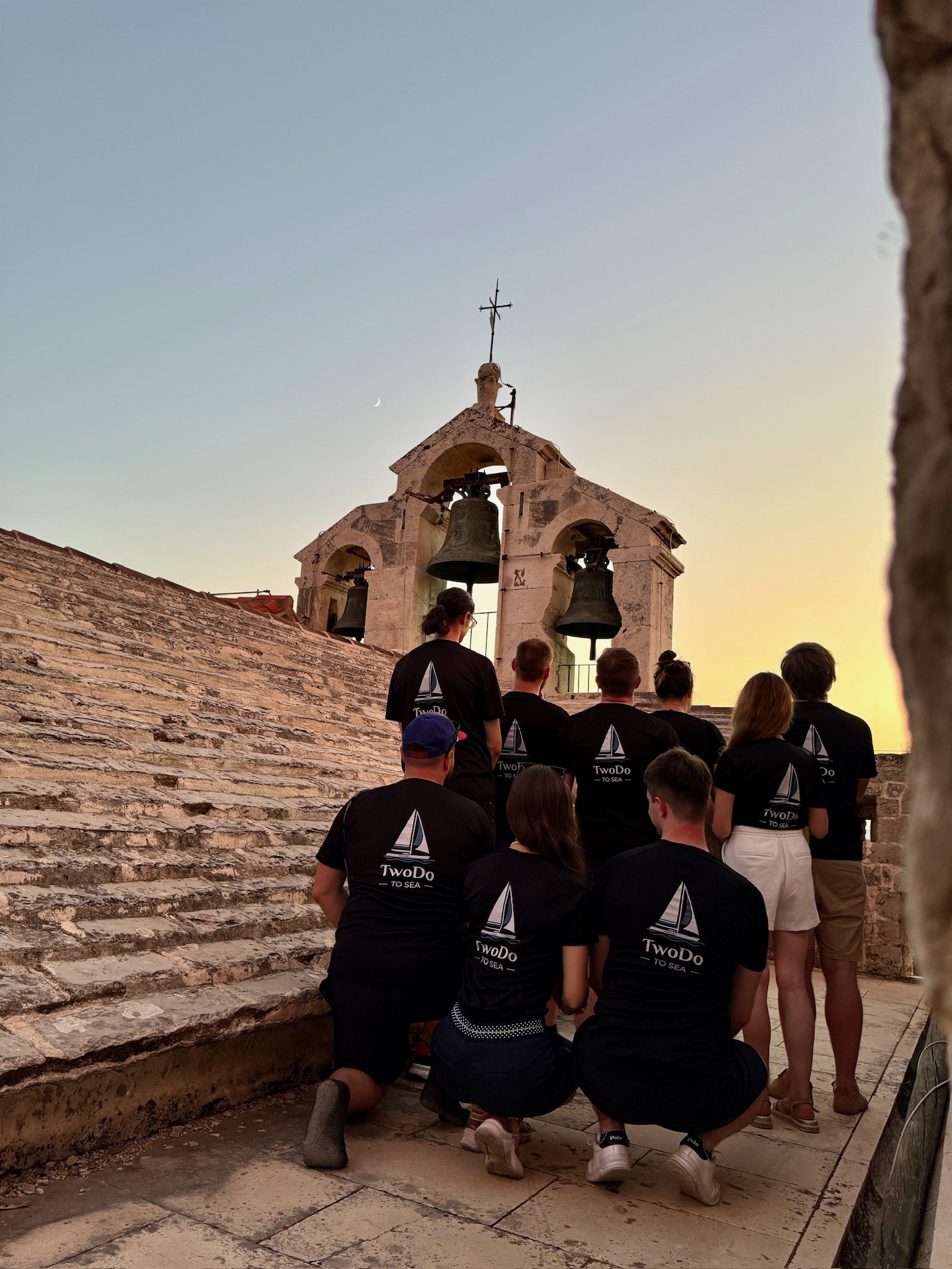 skupina lidí klečících na kamenném schodišti s zvonky