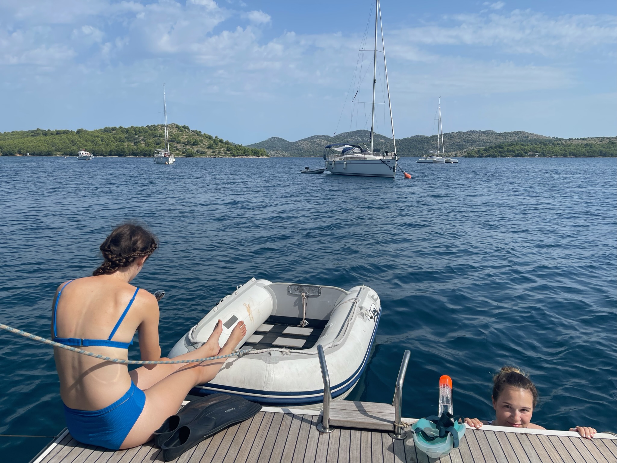 skupina lidí sedící na molu s loděmi ve vodě