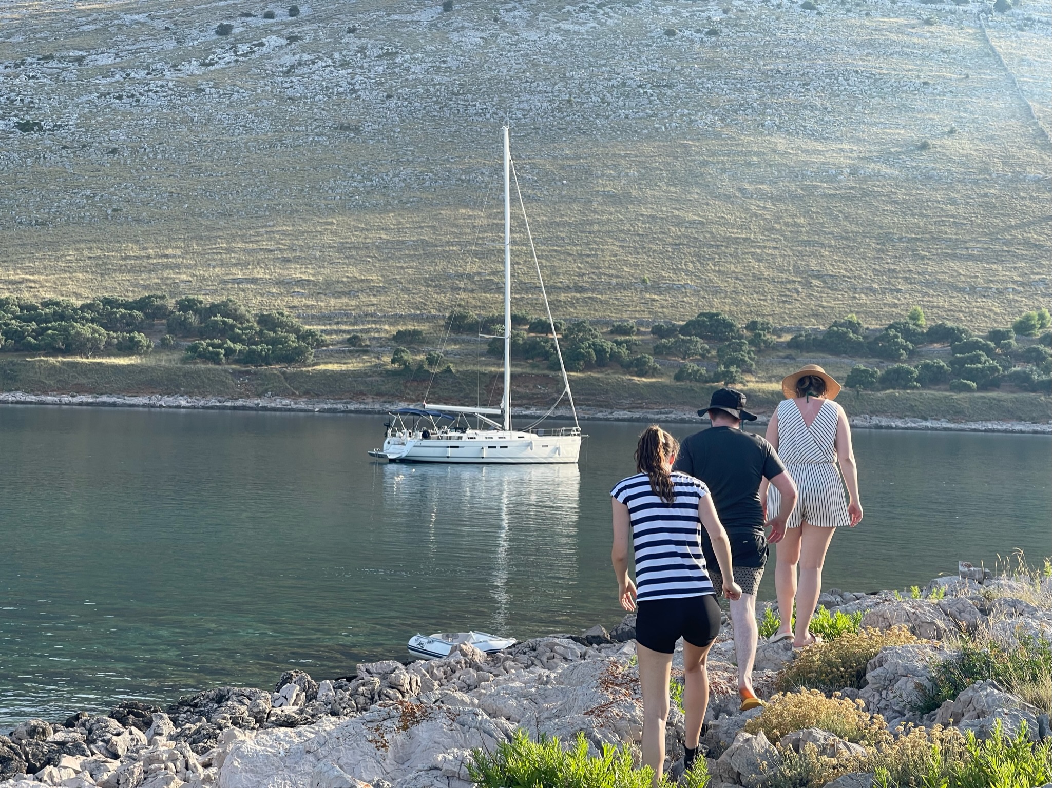 skupina lidí kráčejících po skalnatém břehu s plachetnicí v pozadí